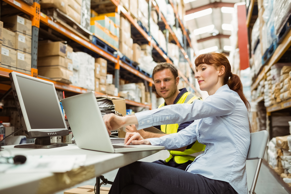 Warehouse worker and manager looking at laptop in a large warehouse